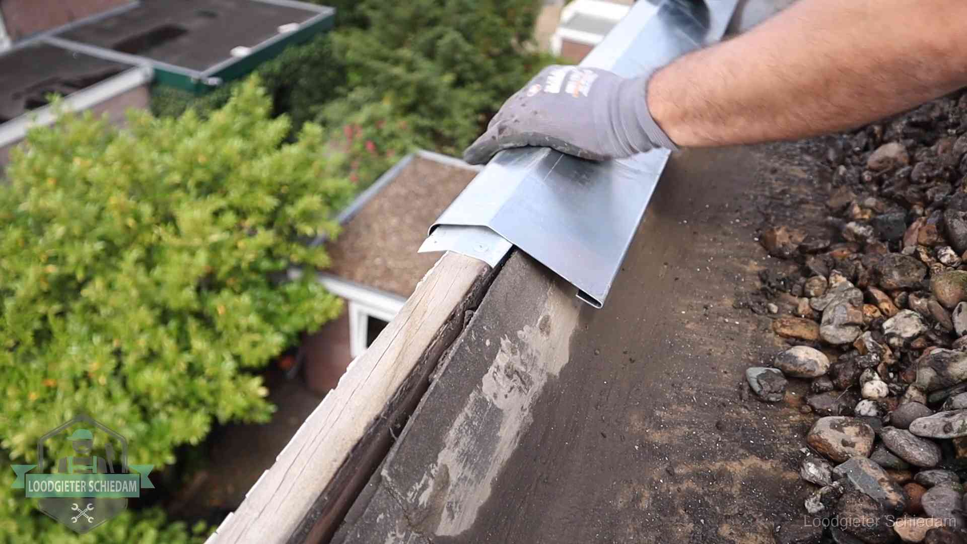 Daklekkage per wijk in Schiedam Dakdekker plaatst een zinken deklijst op een dakrand met uitzicht over een woonwijk in Schiedam