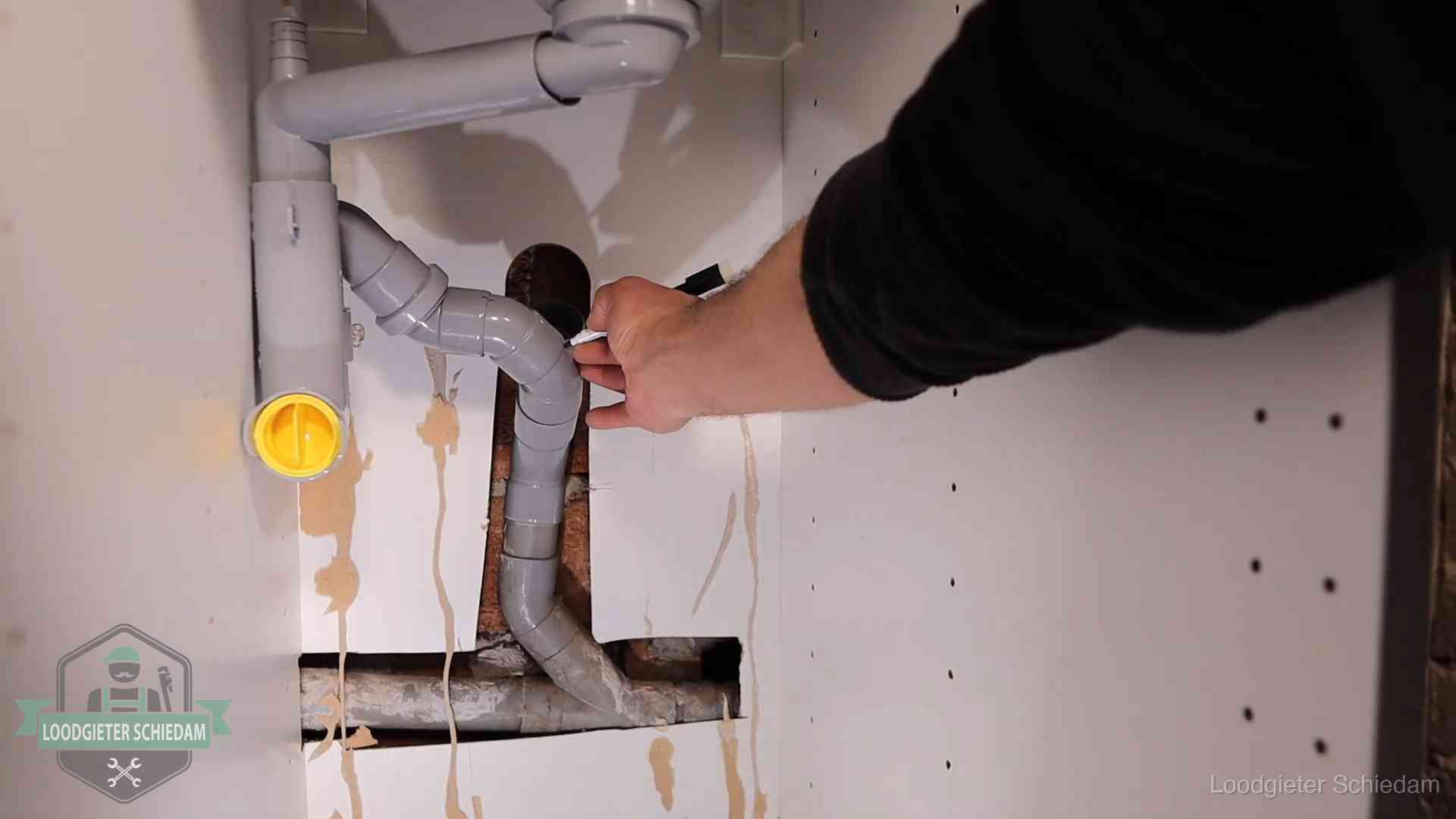 Loodgieter markeert een pvc-afvoerbuis onder een gootsteen in Schiedam