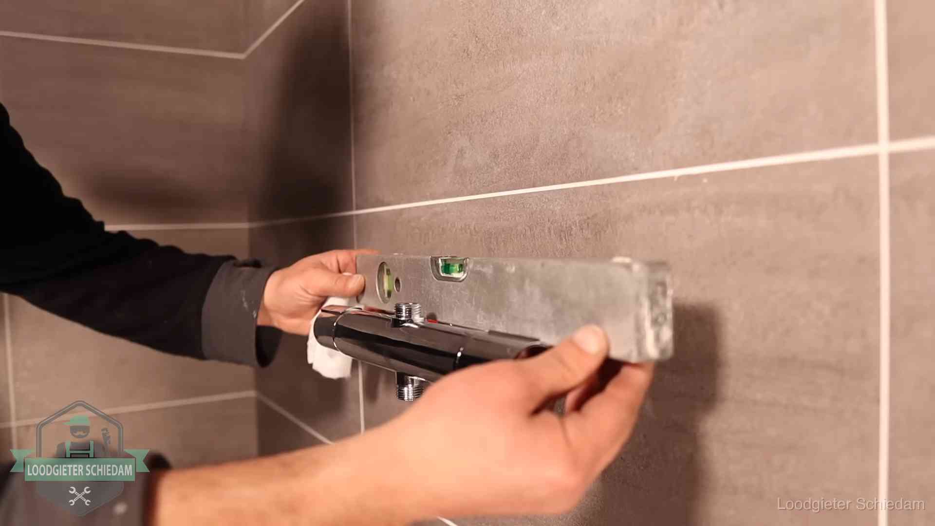 Loodgieter lijnt een douchekraan uit met een waterpas in een woning in Schiedam