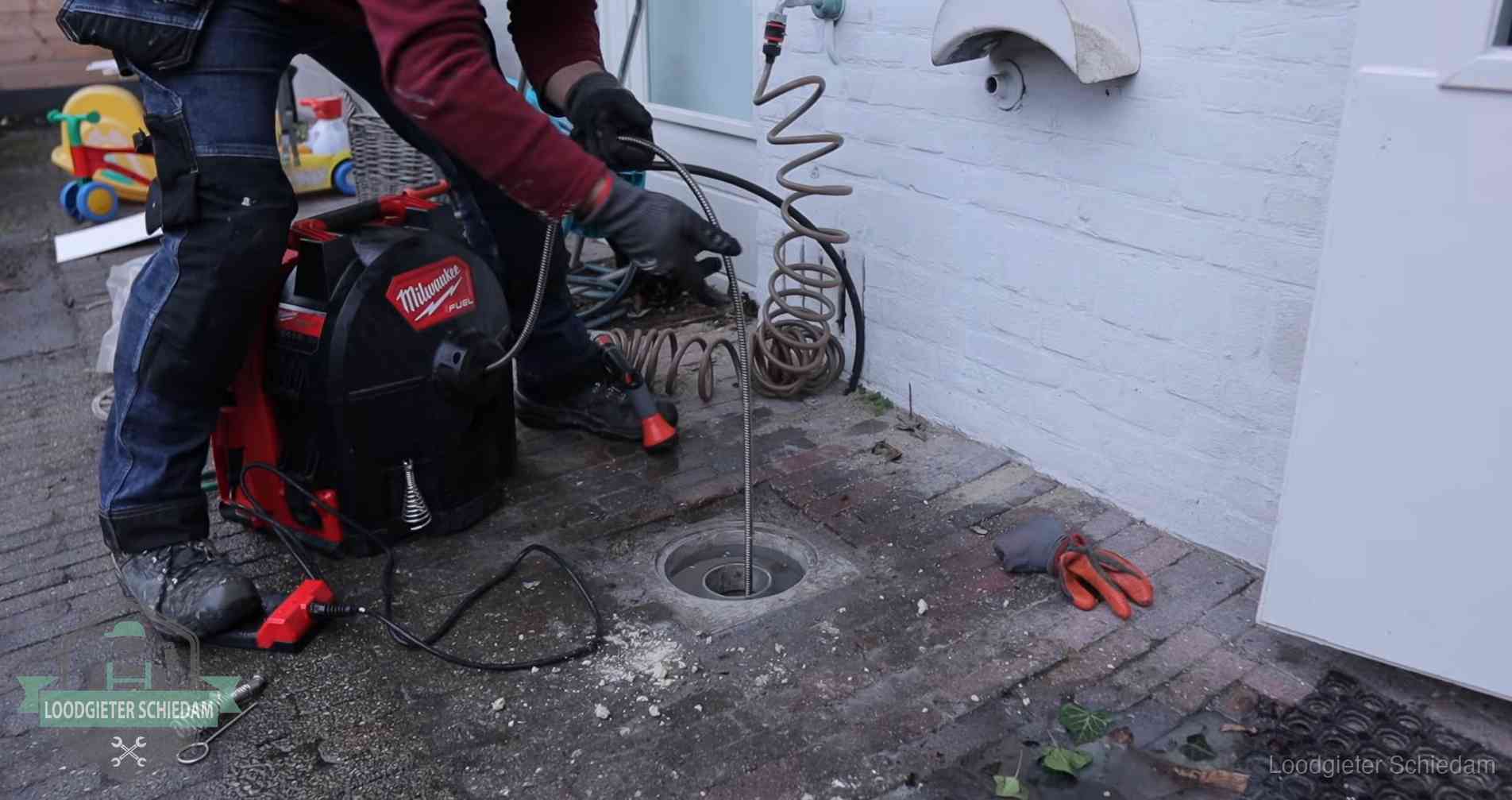 Ontstoppingsputje in de bestrating naast de gevel van een woning in Schiedam