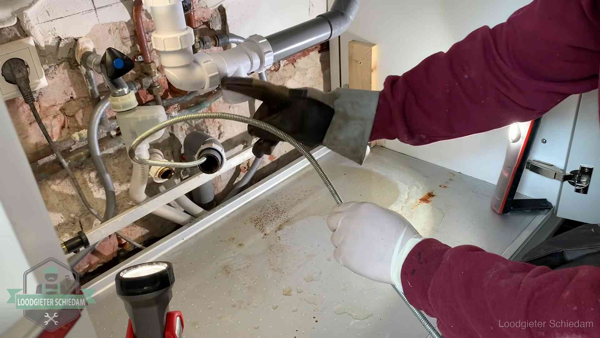 Ontstoppingsveer gaat in een geopende sifonaansluiting onder het aanrecht in Schiedam