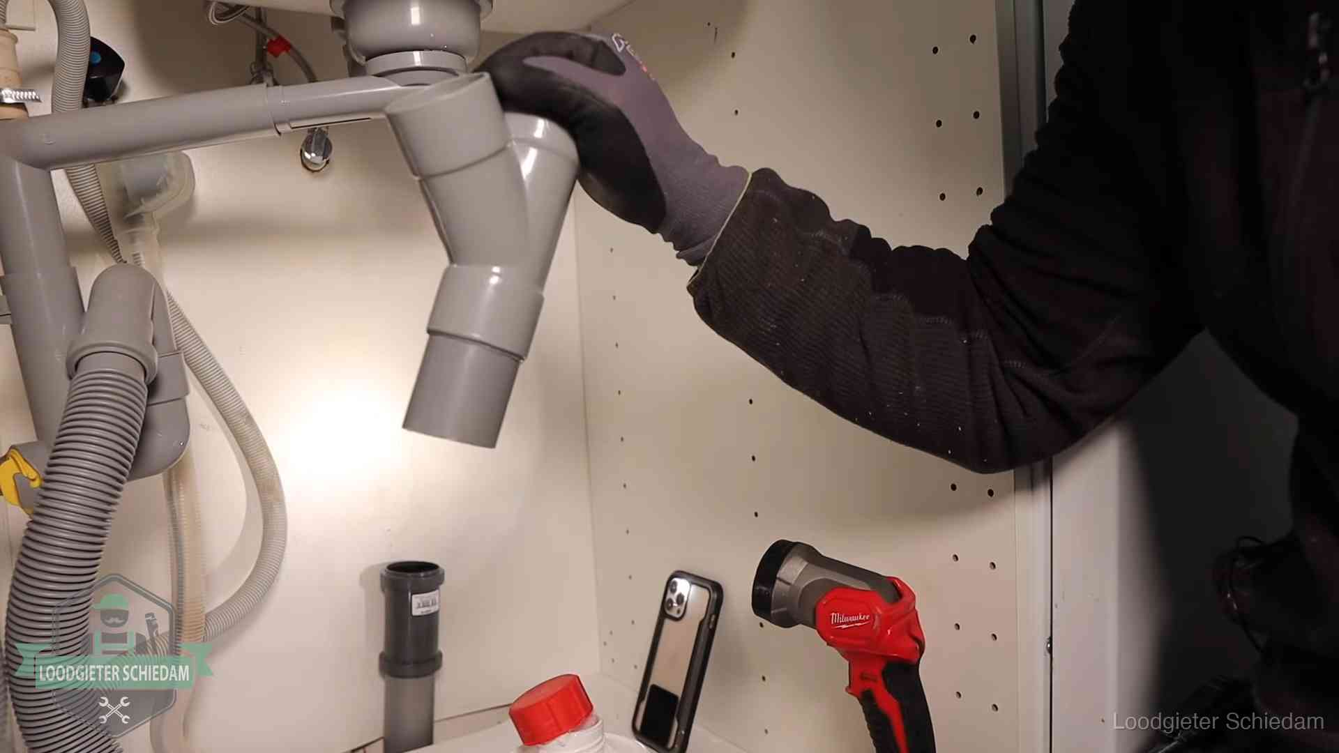 Loodgieter demonteert het sifon- en afvoerwerk onder een gootsteen in Schiedam bij stankklachten