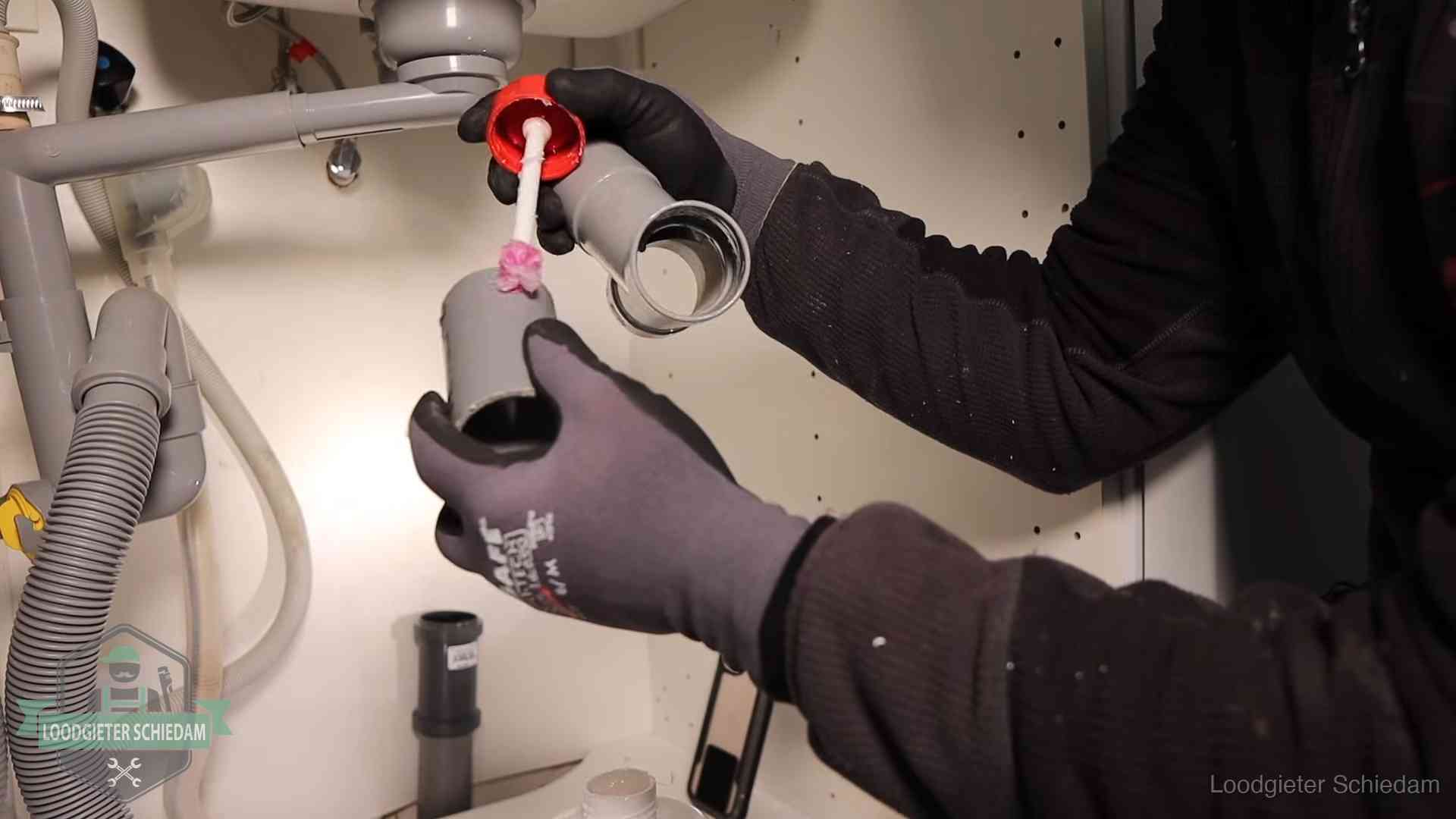 Loodgieter demonteert en reinigt de sifon onder een keukenkast in Schiedam