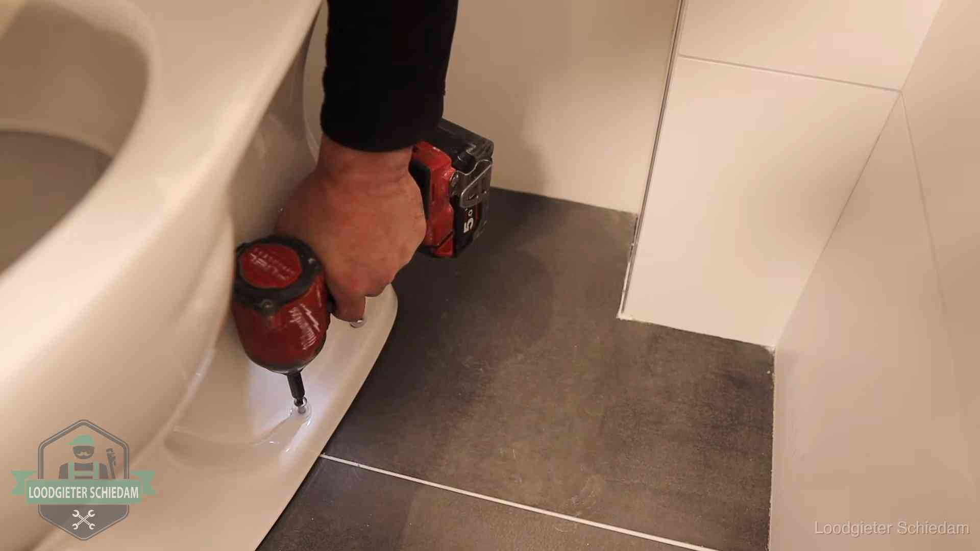 Kosten wc ontstoppen in Schiedam Loodgieter zet de voet van een wc-pot vast op de tegelvloer in Schiedam
